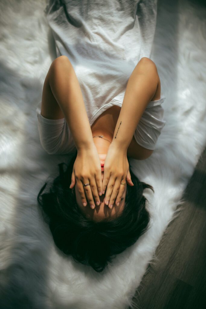 person lying on a bed with their hands over their face
